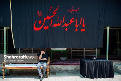 فردی در حال گوش دادن به روضه در حیاط حسینیه است