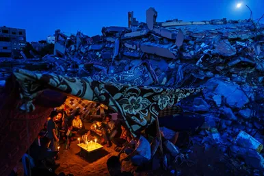 یک خانواده فلسطینی برای محکوم کردن کشتار کودکان و غیرنظامیان در میان بقایای خانه‌هایی در شهر غزه که توسط حمله نظامی اسرائیل در جریان درگیری مسلحانه ۱۱ روزه در ماه مه ویران شده بود، شمع روشن می‌کنند. (مارکوس یام)
